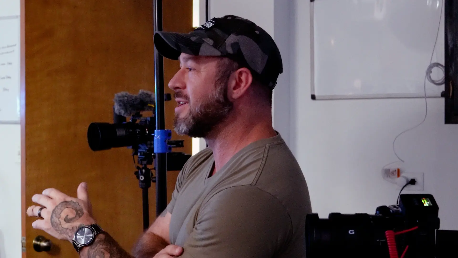 Brad in a cap talking during a production session, with cameras and a microphone set up behind him